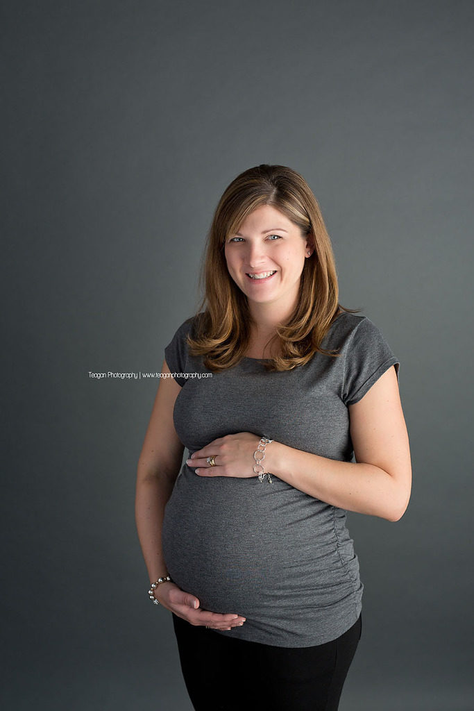 A mother in a grey shirt hugs her pregnant belly suring an Edmonton studio maternity session