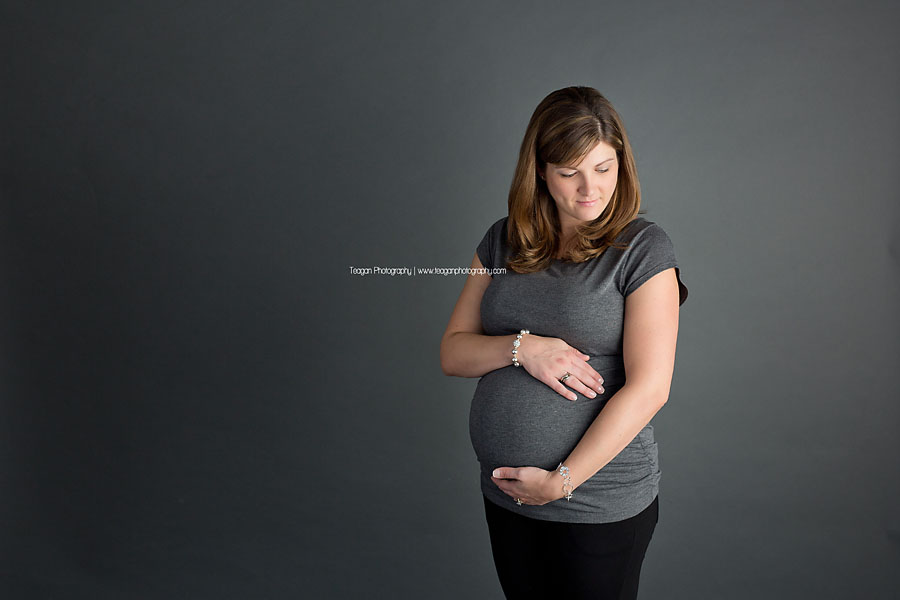 A mother in a grey shirt hugs her pregnant belly suring an Edmonton studio maternity session