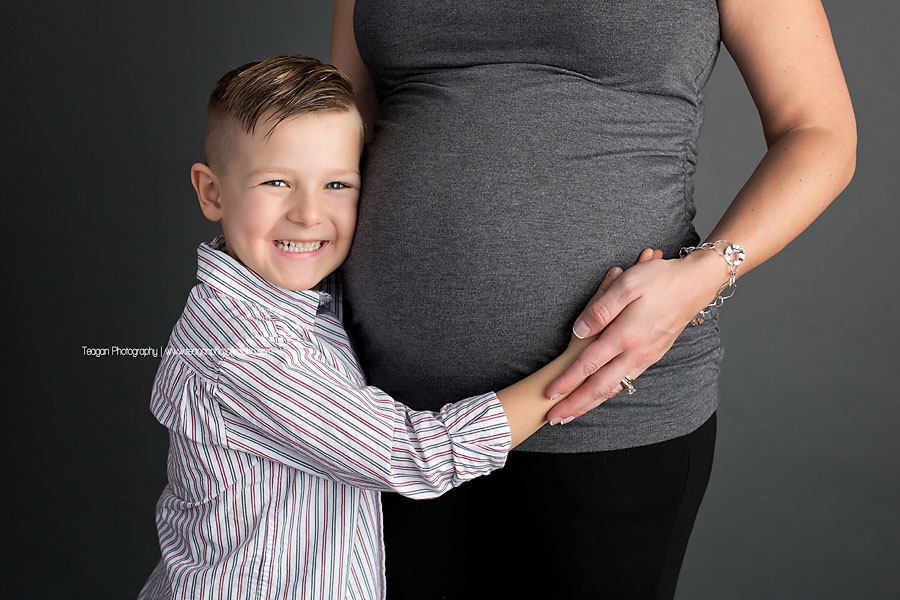 A cheeky smile from a little boy hugging his mom's pregnant belly