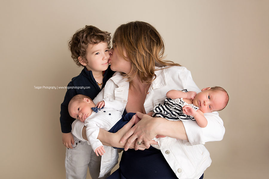 A new mom holds her twin babies while kissing her older son