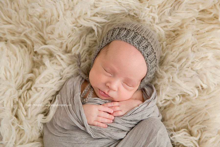 A baby boy in a grey knit hat sleeps soundly during a photography session