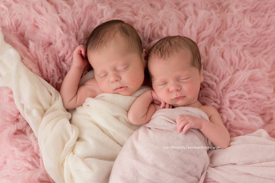 Twin baby girls sleep together on a pink fuzzy rug during an Edmonton twin newborn session