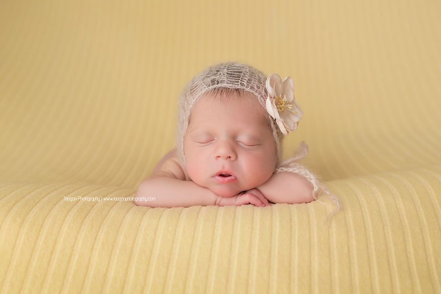 Asleep on a pale yellow blanket and wearing a white knit bonnett is an Edmonton newborn girl