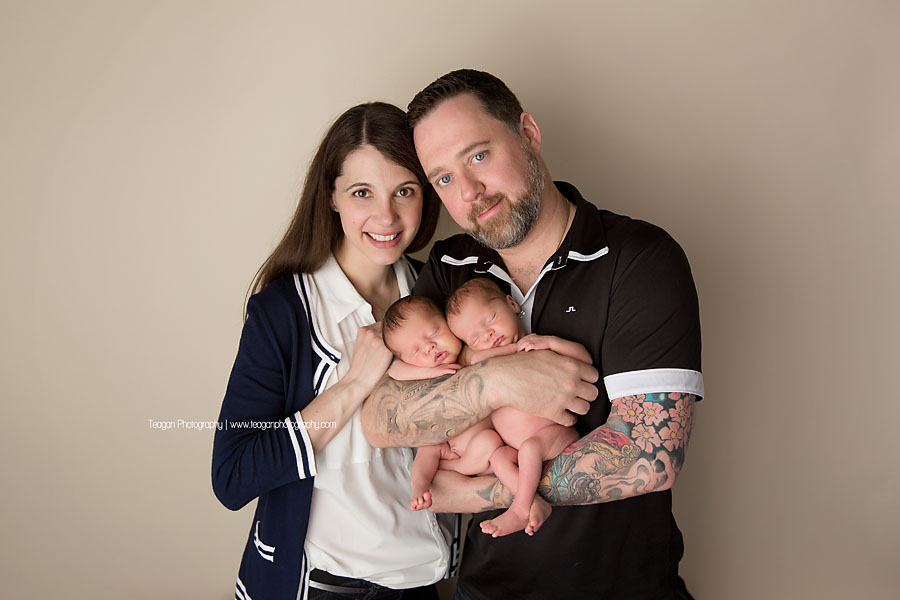 A dark haired couple snuggle together with their newborn twin daughters during an Edmonton photo session