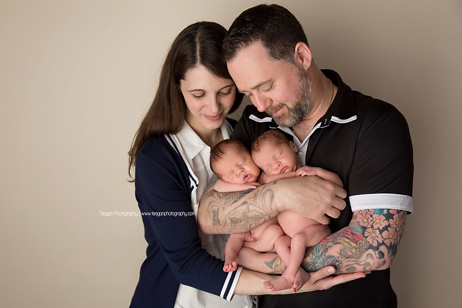 A dark haired couple snuggle together with their newborn twin daughters during an Edmonton photo session