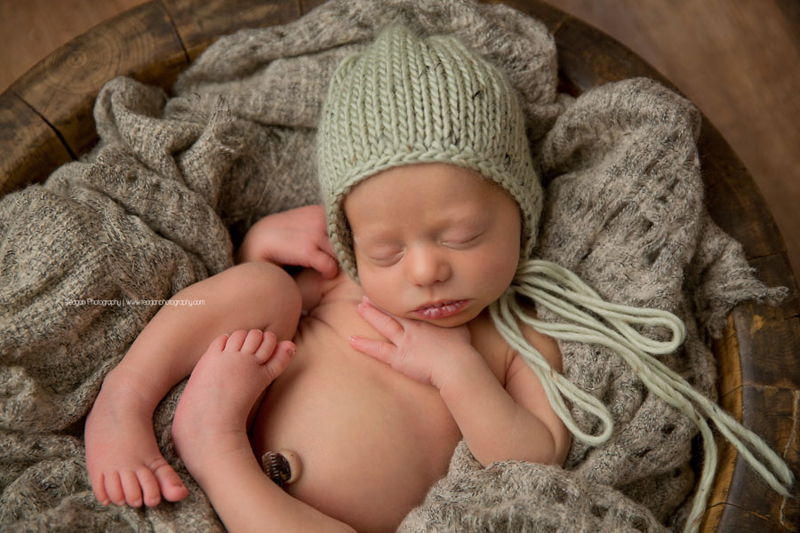 A little baby boy is curled up in a grey blanket and wearing a green knit hat
