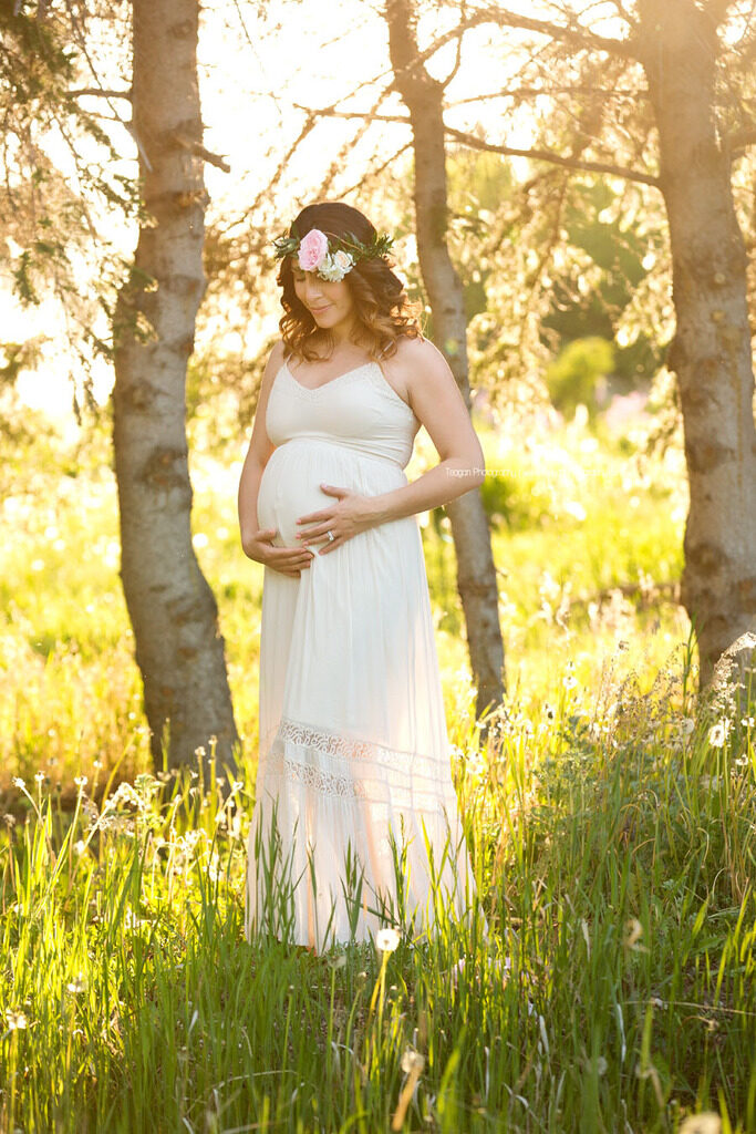 pregnant mother smiling and holding her baby bump during an outdoor Edmonton maternity photography session