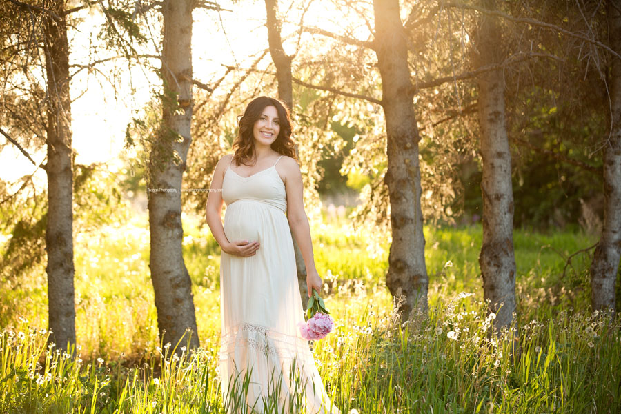 pregnant mother smiling and holding her baby bump during an outdoor Edmonton maternity photography session