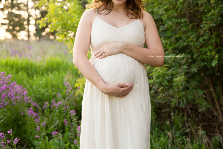 pregnant mother smiling and holding her baby bump during an outdoor Edmonton maternity photography session