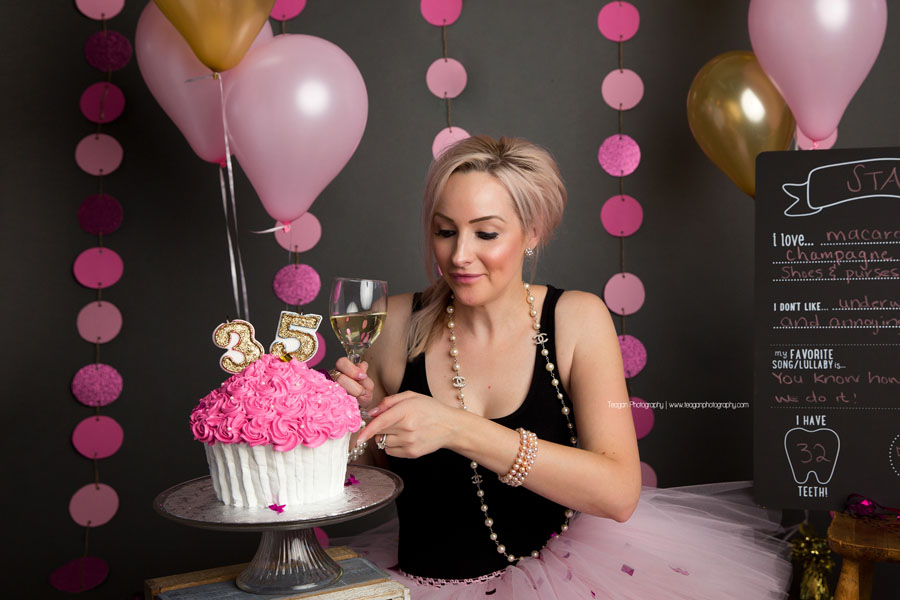 A blonde woman wearing a pink tutu tastes the pink icing on her birthday cake during an adult cake smash photoshoot