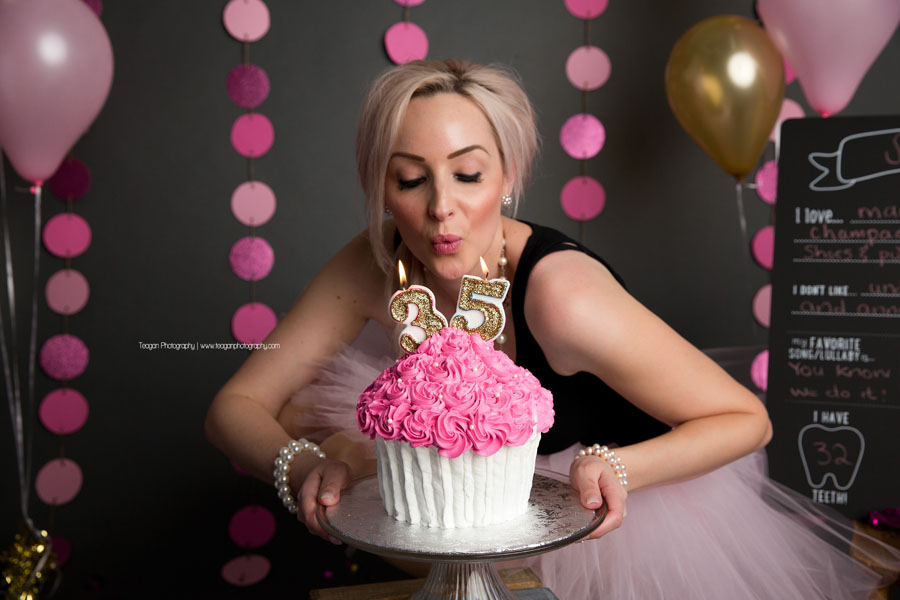 An adult birthday girl blows out the sparkly gold candles on her pink ckae smash cake.