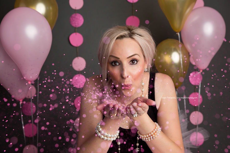 A blonde woman blows pink glitter during her adult cake smash photos in Edmonton