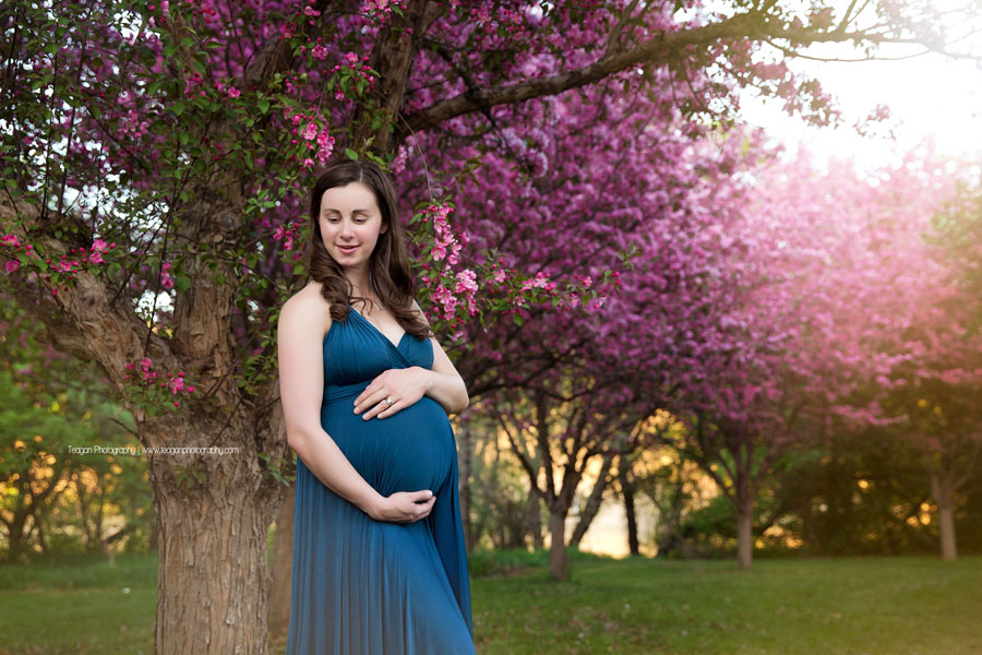 A woman hugs her pregnant belly in front of a blooming cherry tree