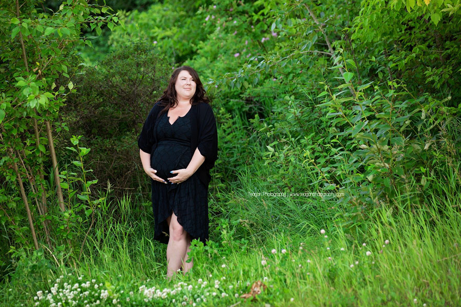 A pregnant Edmonton woman wearing a block dress holds her baby belly  during a maternity photography session