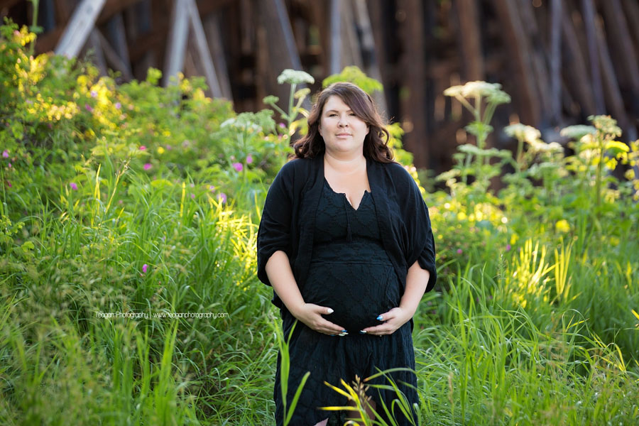 A pregnant Edmonton woman wearing a block dress holds her baby belly  during a maternity photography session