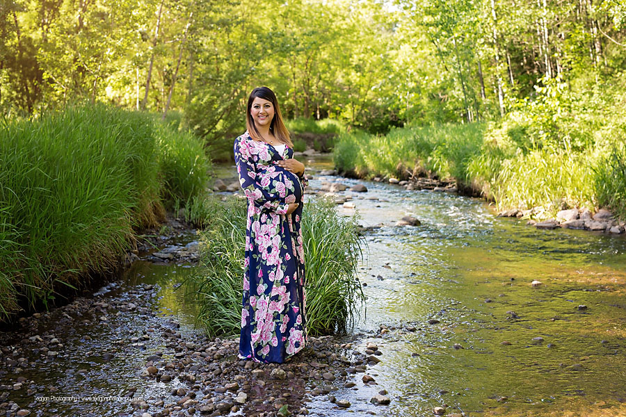 Pregnant mother posing elegantly by a shallow creek in the Edmonton Millcreek ravine during summer