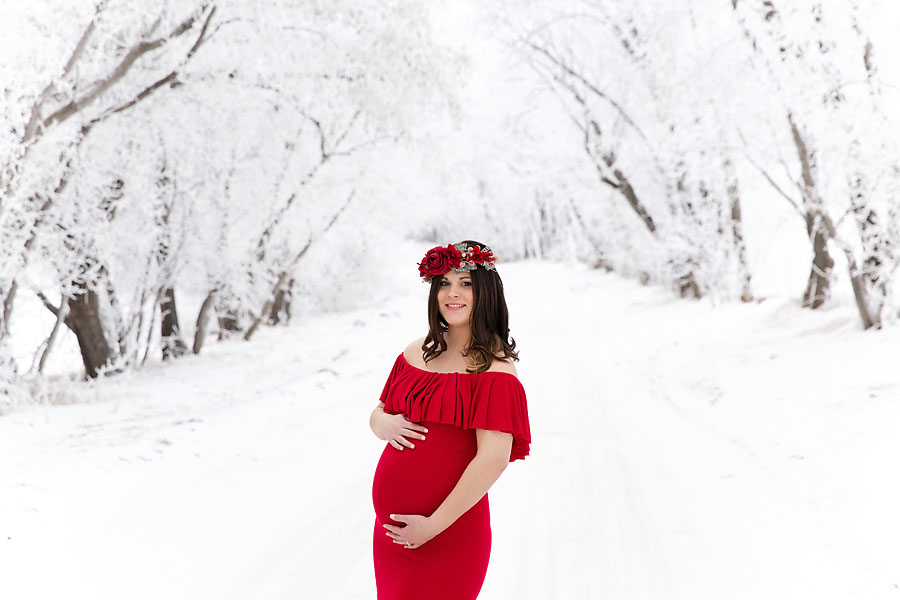 Close up of baby bump on an expecting woman wearing a crimson gown in a snowy Edmonton park