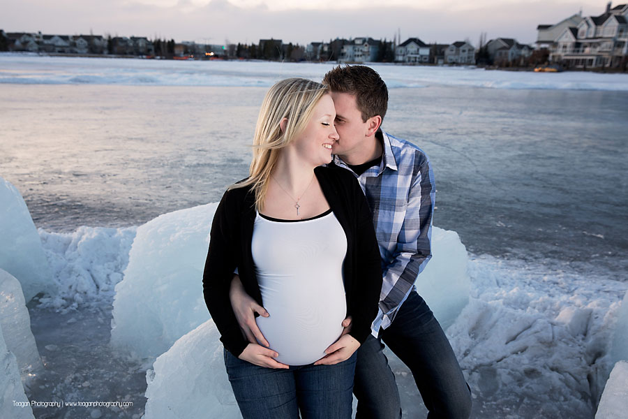 Pregnant mother and husband posing at sunset in front of Lake Summerside in Edmonton during a winter maternity session