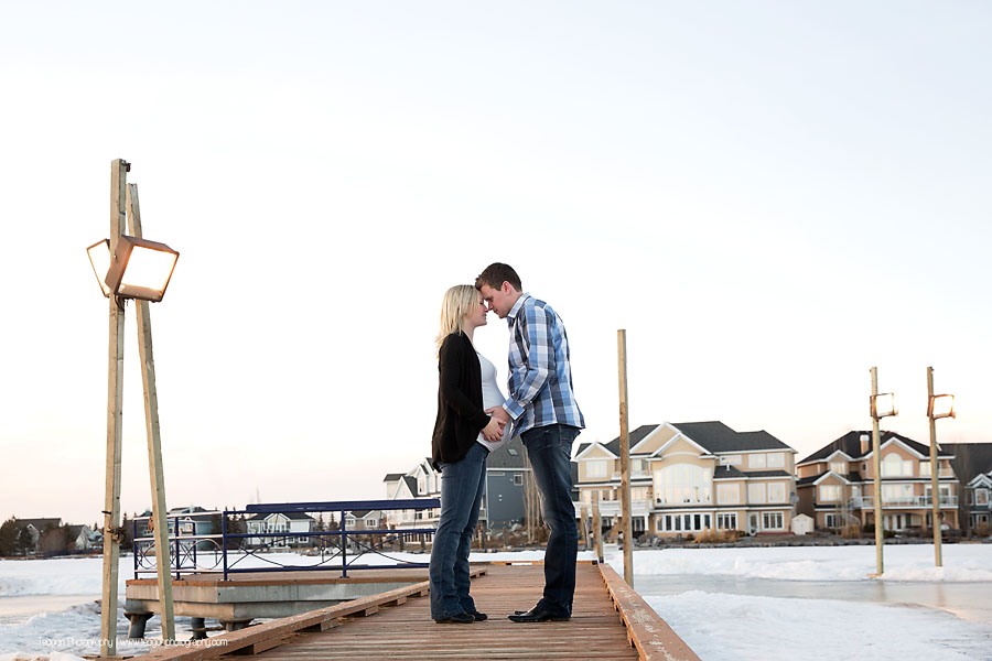 Pregnant mother and husband posing at sunset in front of Lake Summerside in Edmonton during a winter maternity session