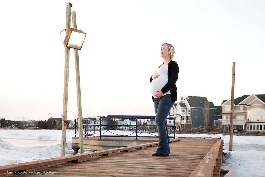 Outdoor winter pregnancy photos featuring a couple in front of frozen Lake Summerside landscape