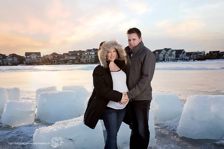Pregnant mother and husband posing at sunset in front of Lake Summerside in Edmonton during a winter maternity session