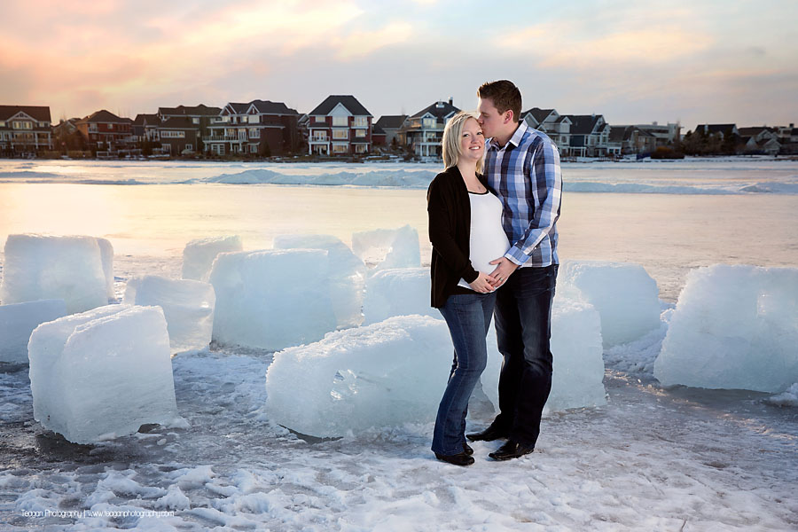 Pregnant mother and husband posing at sunset in front of Lake Summerside in Edmonton during a winter maternity session
