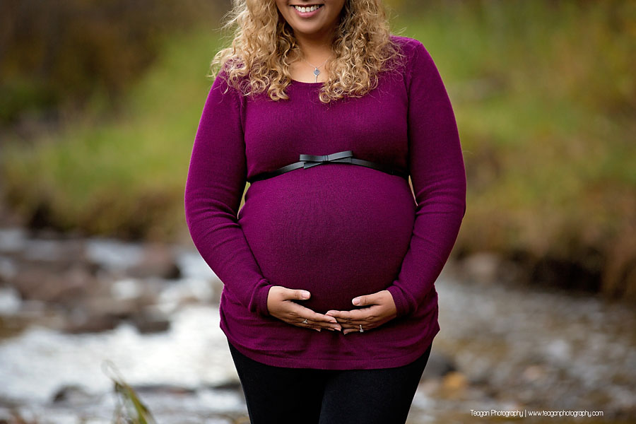Pregnant mother walking along a rocky creek bed surrounded by golden autumn leaves in an Edmonton ravine