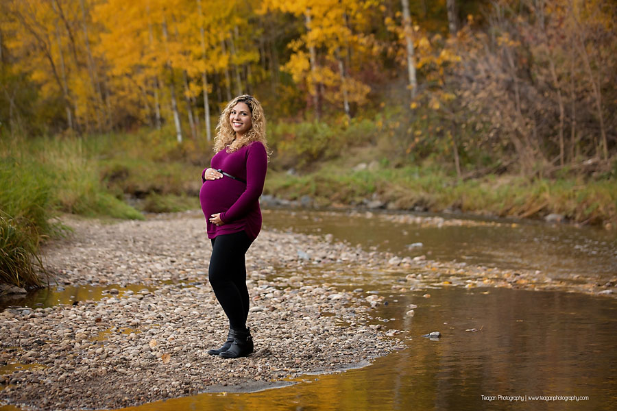 Pregnant mother walking along a rocky creek bed surrounded by golden autumn leaves in an Edmonton ravine