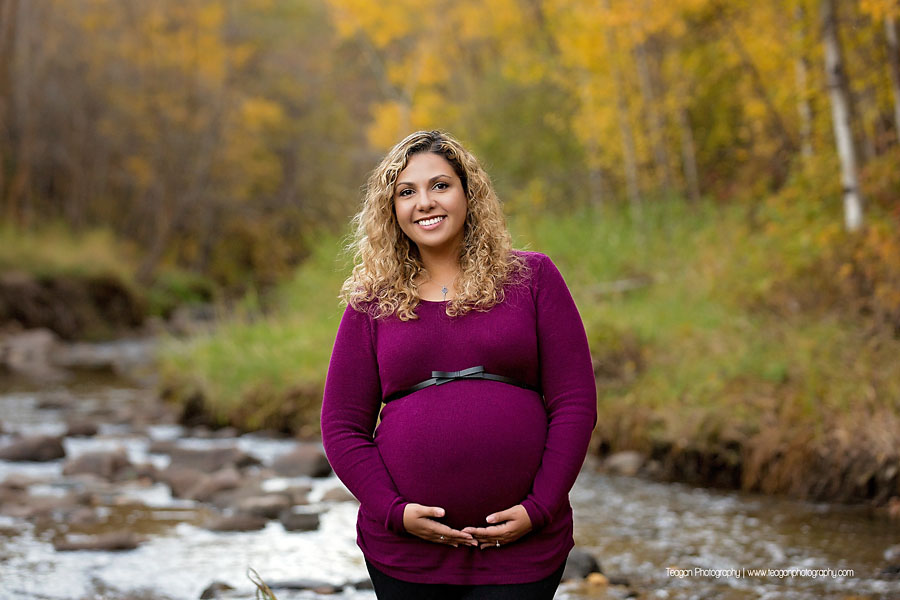 Pregnant mother walking along a rocky creek bed surrounded by golden autumn leaves in an Edmonton ravine
