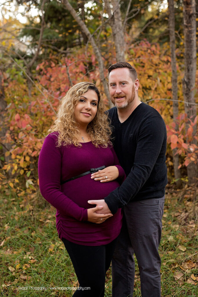 Close up of baby bump with a crisp running stream and colorful autumn leaves in the background in Edmonton