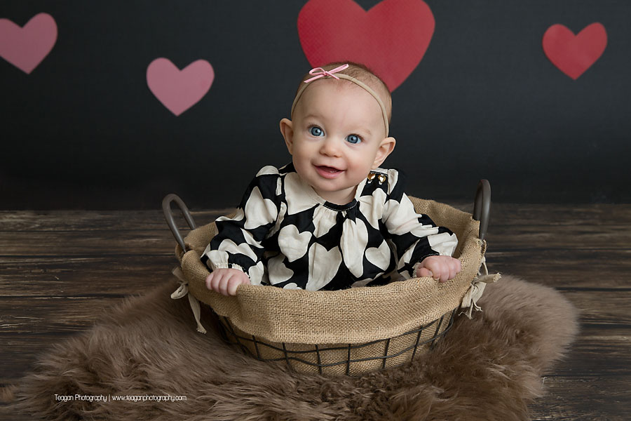Sitting in a wire basket is a baby girl during a Valentine's Mini photoshoot in Edmonton